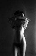 A knit shirt, mid-removal. Arms tangled overhead, face absorbed into cloth — the figure caught in the precise second when identity goes quiet and the body speaks alone. The torso holds the frame; everything above dissolves.